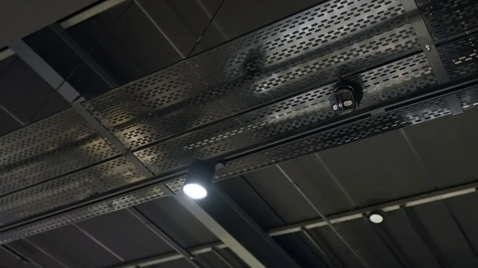 CCTV dome camera mounted on a black cable tray under a store ceiling