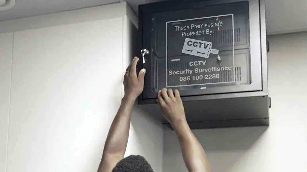 CCTV Security Surveillance technician closing a wall-mounted CCTV cabinet marked 'These premises are protected by CCTV Security Surveillance'