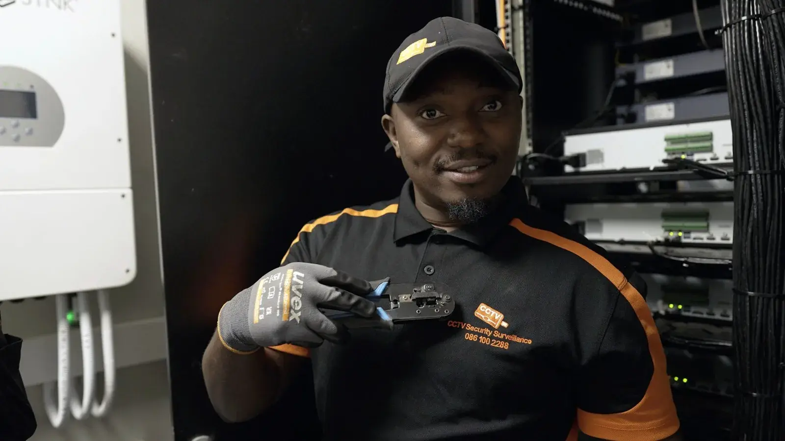 CCTV Security Surveillance technician holding a network crimping tool beside a solar inverter and a CCTV recorder rack
